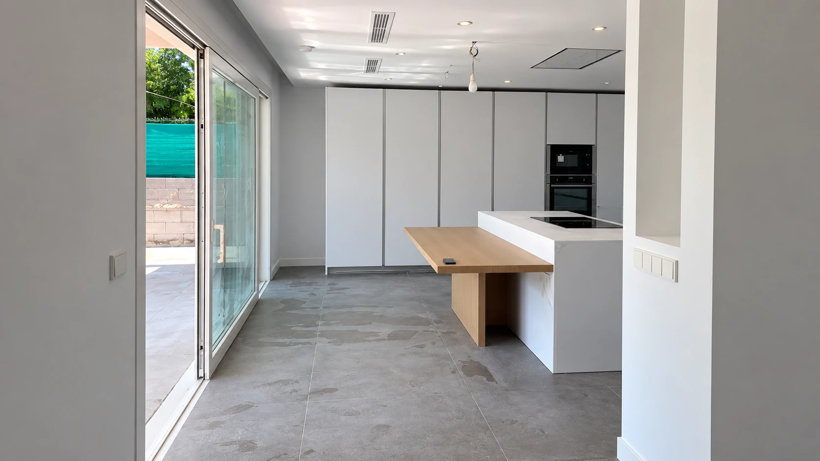 Vista de una cocina con muebles blancos, barra de madera y ventanal al jardín
