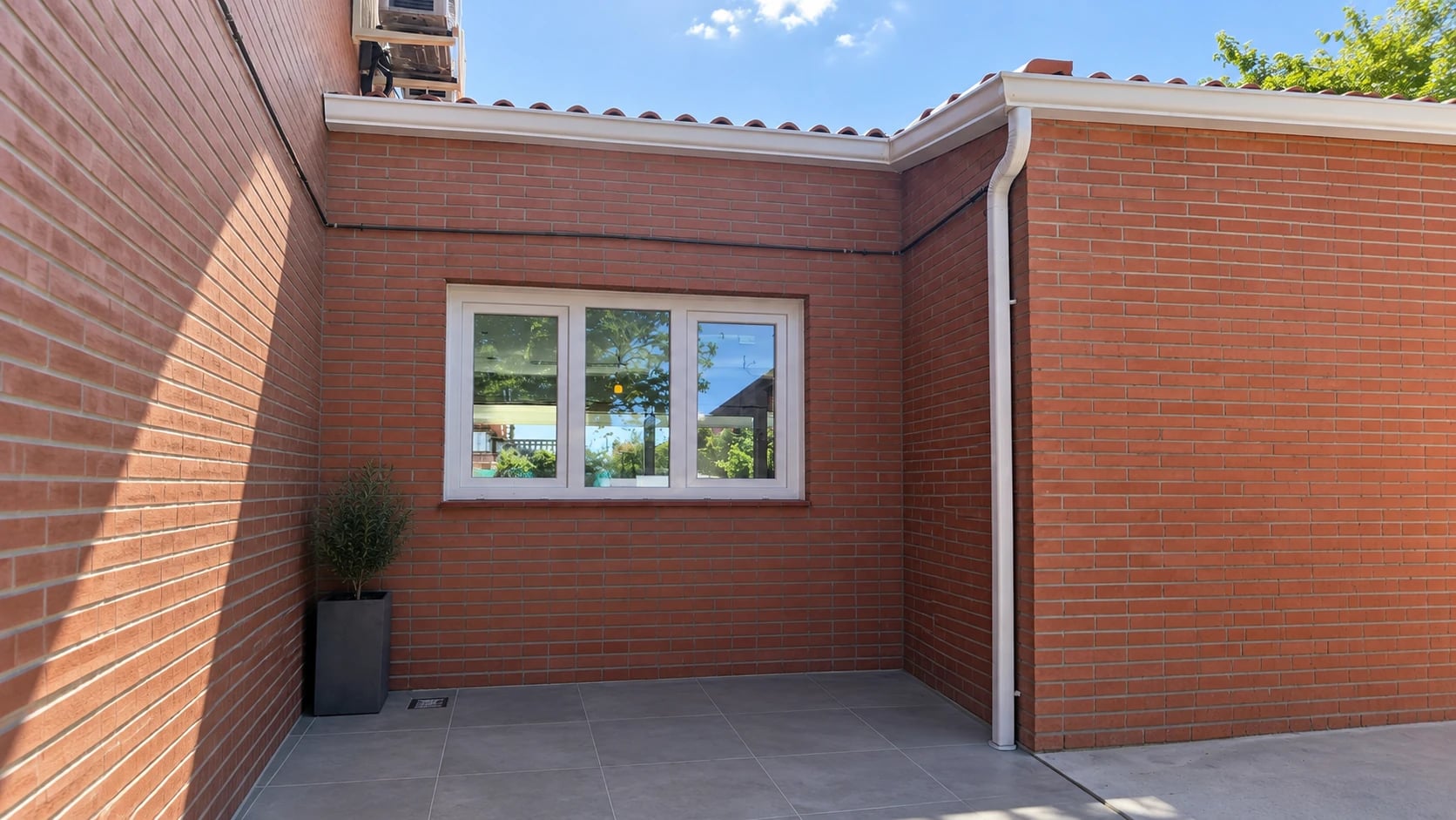 Patio terminado con pavimento gris, fachada de ladrillo y ventana blanca